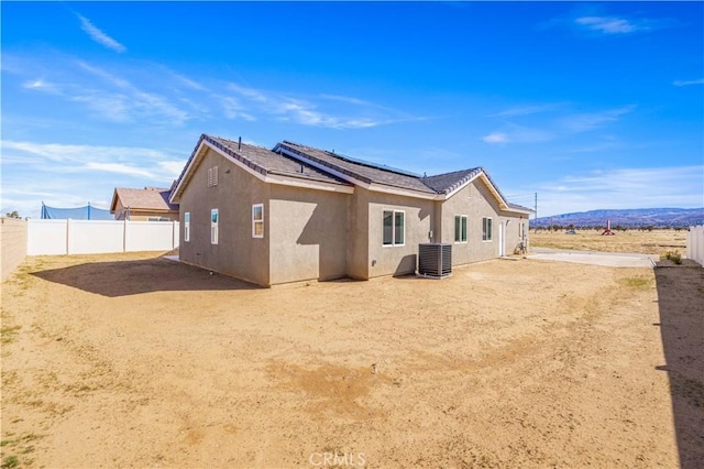 back of property featuring solar panels, central AC, a fenced backyard, and stucco siding