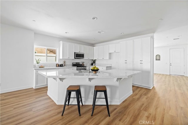 5651 W W Ave Unit J15, Lancaster, CA 93536 - kitchen with stainless steel appliances, white cabinets, a kitchen island with sink, light wood-type flooring, and a kitchen breakfast bar