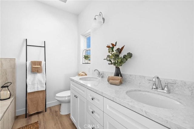 bathroom featuring double vanity, a sink, toilet, and wood finished floors