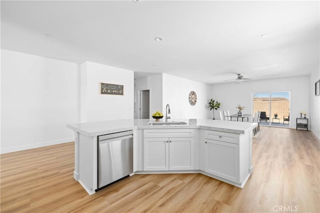 kitchen with a kitchen island with sink, light countertops, light wood-type flooring, stainless steel dishwasher, and a sink