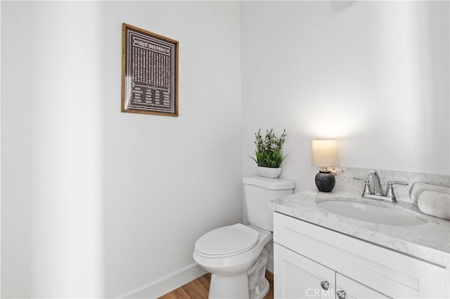 bathroom featuring toilet, baseboards, wood finished floors, and vanity