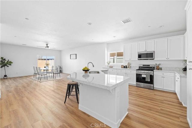 kitchen featuring light wood finished floors, a center island with sink, white cabinets, appliances with stainless steel finishes, and a sink