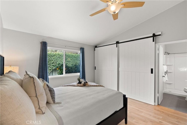 bedroom with a barn door, lofted ceiling, ceiling fan, light wood-style flooring, and ensuite bath