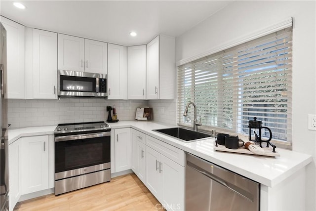 kitchen with stainless steel appliances, a sink, light wood-style floors, white cabinets, and tasteful backsplash