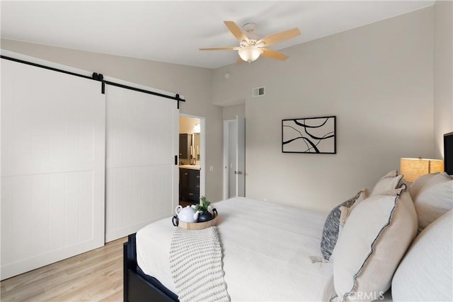 bedroom with a barn door, visible vents, light wood-style floors, vaulted ceiling, and ensuite bath