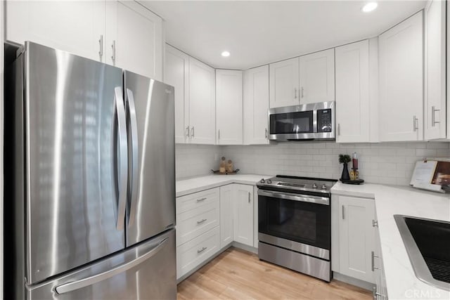 kitchen featuring light wood-style flooring, stainless steel appliances, a sink, white cabinets, and backsplash