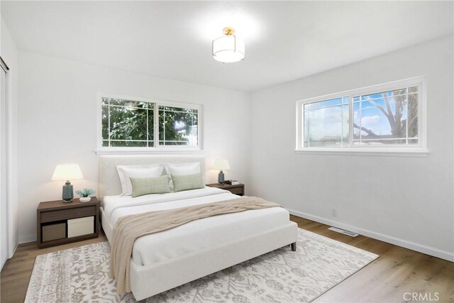 bedroom with multiple windows, wood finished floors, visible vents, and baseboards