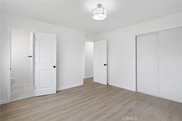 unfurnished bedroom featuring a closet, baseboards, ensuite bath, and wood finished floors