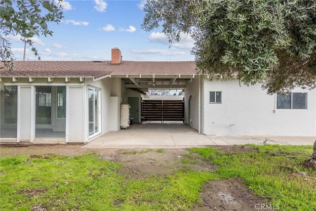 back of property featuring a carport, a chimney, roof with shingles, and stucco siding