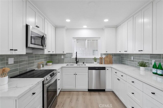 kitchen featuring stainless steel appliances, white cabinets, a sink, and light wood-style flooring