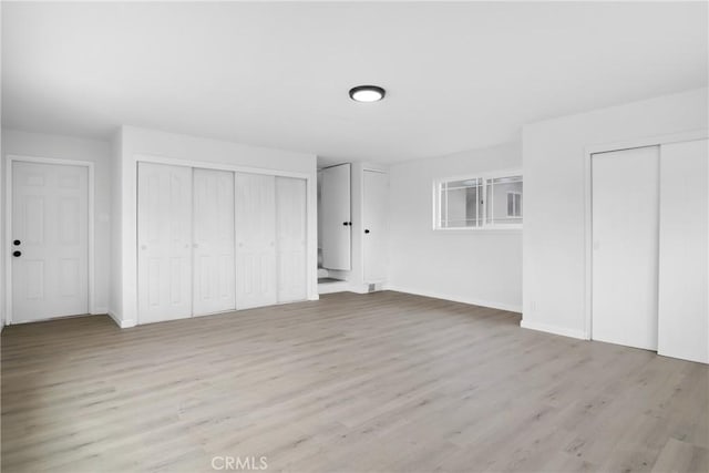 unfurnished bedroom with baseboards, two closets, and wood finished floors