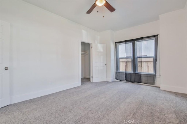 carpeted empty room with ornamental molding, a ceiling fan, and baseboards