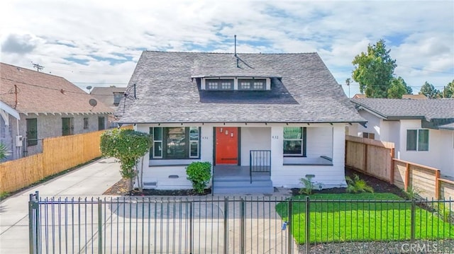 bungalow-style house with a fenced front yard, roof with shingles, and a front lawn