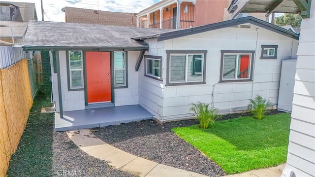 doorway to property featuring roof with shingles and fence