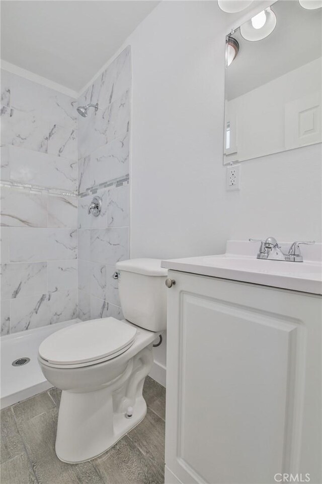 bathroom with wood finish floors, toilet, ornamental molding, a stall shower, and vanity