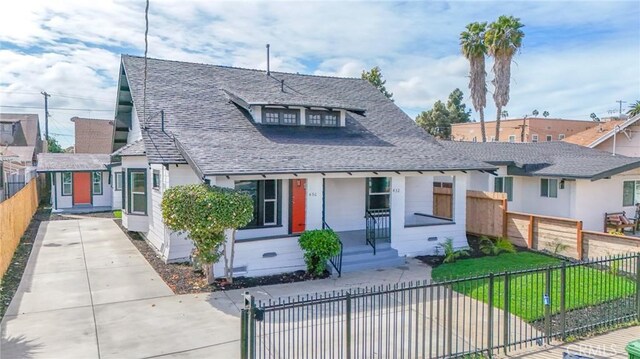 view of front facade featuring a fenced front yard, a shingled roof, driveway, and a front lawn