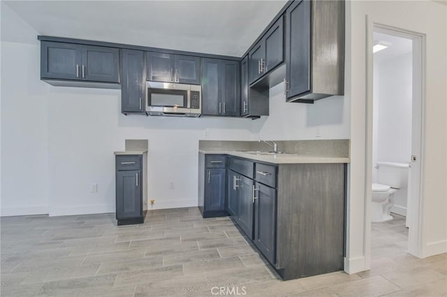 kitchen with light countertops, stainless steel microwave, wood tiled floor, a sink, and baseboards