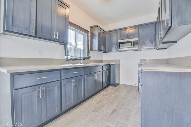 kitchen featuring light countertops, wood finish floors, stainless steel microwave, and a sink