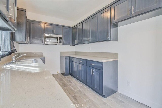 kitchen featuring light stone counters, wood finish floors, stainless steel microwave, a sink, and baseboards