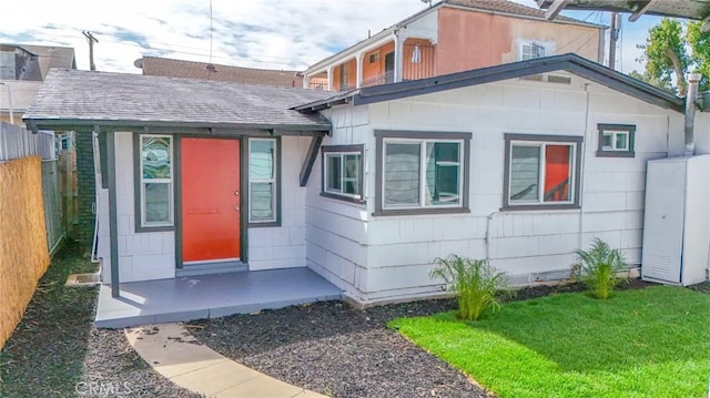 property entrance with roof with shingles, fence, and a lawn