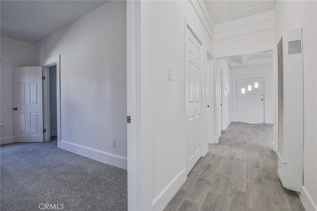 corridor featuring a heating unit, beamed ceiling, baseboards, and wood finished floors