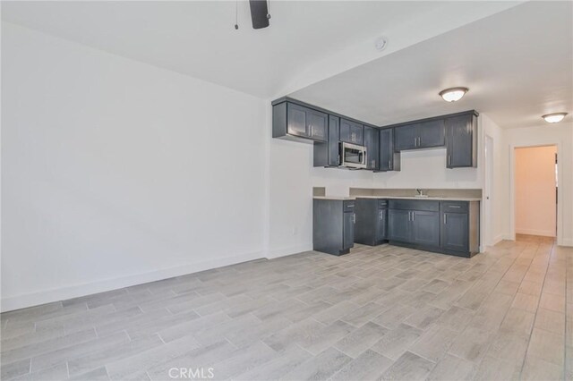 kitchen featuring light wood finished floors, baseboards, a ceiling fan, stainless steel microwave, and light countertops