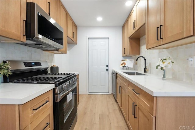 kitchen featuring tasteful backsplash, light wood-style flooring, appliances with stainless steel finishes, light countertops, and a sink