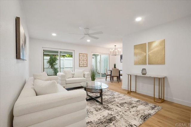 living room featuring baseboards, ceiling fan with notable chandelier, light wood-type flooring, and recessed lighting