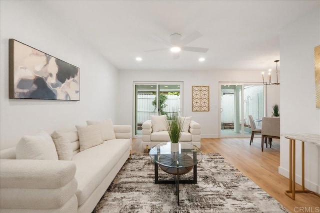 living area featuring light wood-style floors, ceiling fan with notable chandelier, baseboards, and recessed lighting