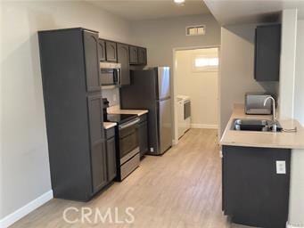 kitchen with light countertops, appliances with stainless steel finishes, light wood-style floors, a sink, and independent washer and dryer