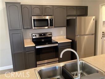 kitchen with gray cabinets, light countertops, appliances with stainless steel finishes, a sink, and baseboards