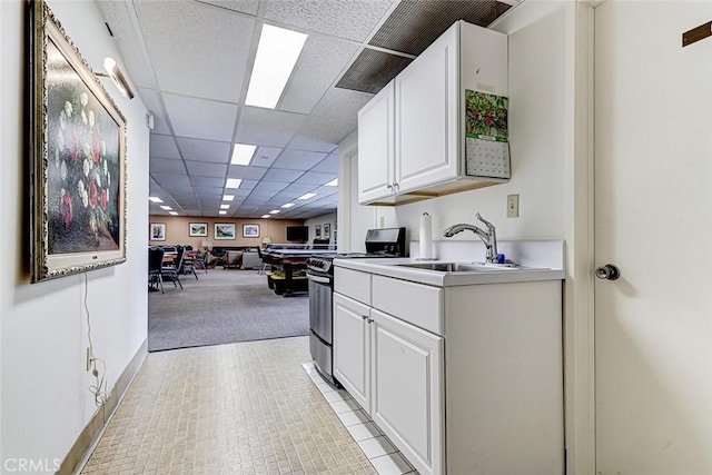 kitchen featuring a drop ceiling, light countertops, stainless steel range with electric cooktop, white cabinetry, and a sink