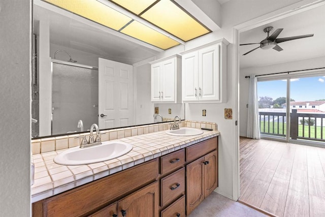 bathroom featuring ceiling fan, double vanity, walk in shower, and a sink