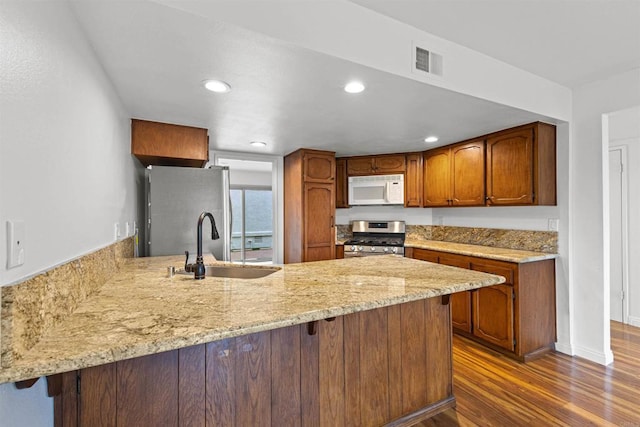 kitchen with visible vents, a peninsula, a sink, dark wood-type flooring, and appliances with stainless steel finishes