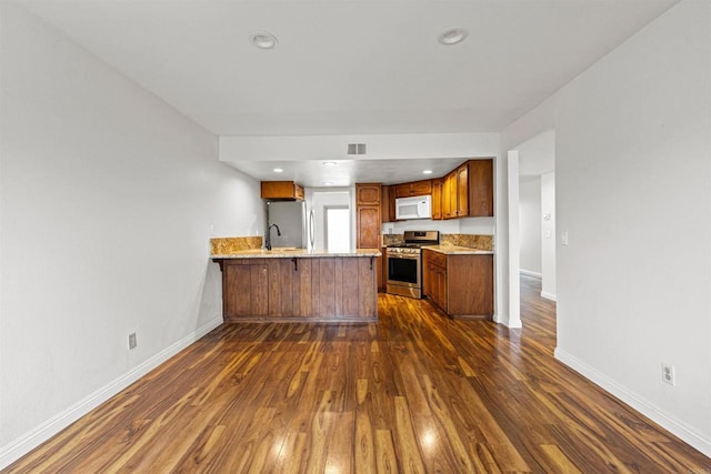 kitchen featuring dark wood finished floors, appliances with stainless steel finishes, a peninsula, brown cabinetry, and light countertops