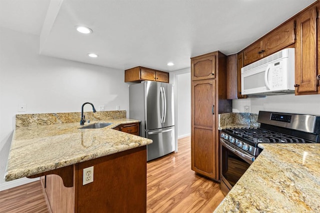 kitchen featuring light stone countertops, light wood-style flooring, a peninsula, stainless steel appliances, and a sink