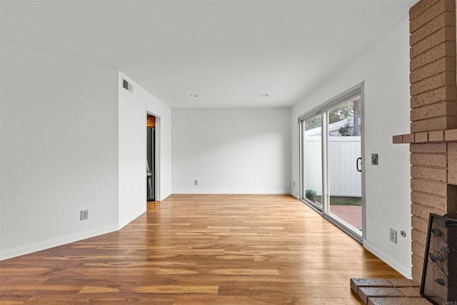 unfurnished living room featuring visible vents, light wood-style flooring, a brick fireplace, and baseboards