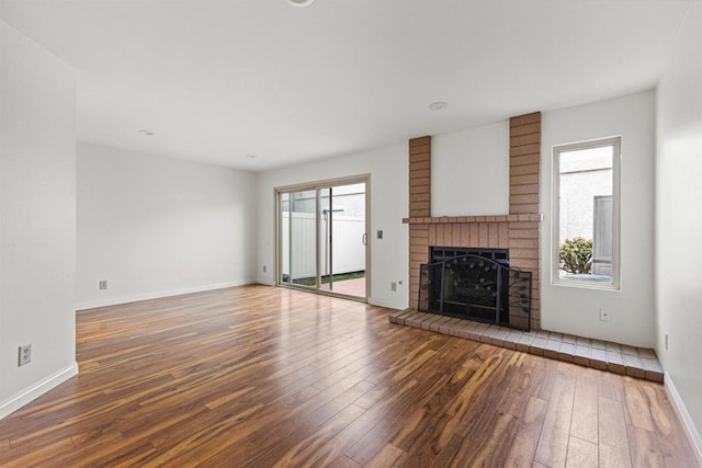 unfurnished living room featuring a wealth of natural light, wood-type flooring, and a brick fireplace