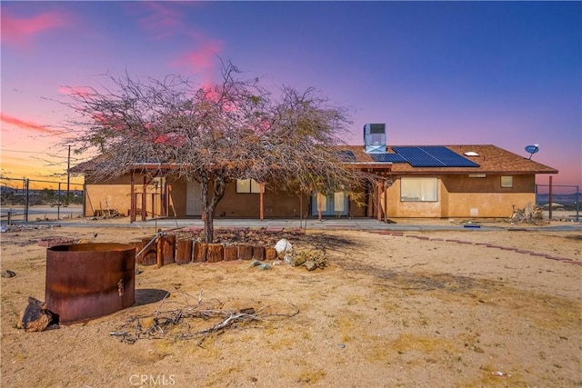 back of house at dusk with stucco siding, fence, and solar panels