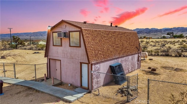 view of property exterior featuring roof with shingles, fence, a mountain view, and a gambrel roof