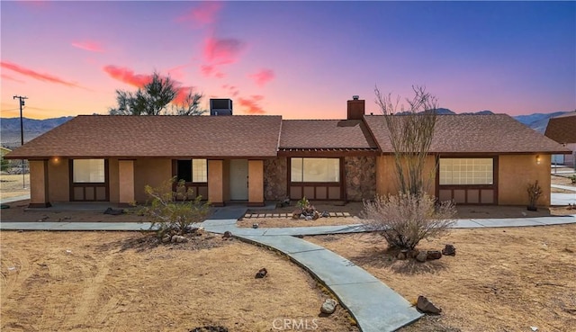 ranch-style home featuring covered porch, roof with shingles, and stucco siding