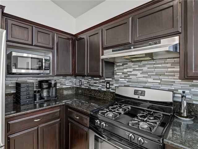 kitchen with dark brown cabinetry, under cabinet range hood, appliances with stainless steel finishes, decorative backsplash, and dark stone countertops