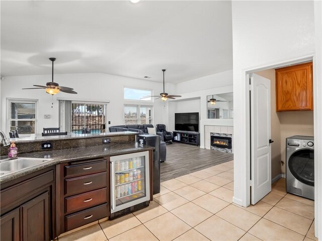 kitchen featuring lofted ceiling, wine cooler, light tile patterned flooring, a sink, and washer / dryer