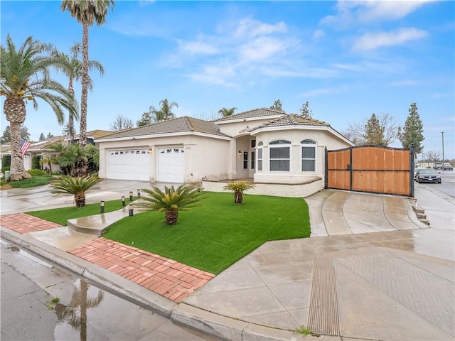 mediterranean / spanish home featuring concrete driveway, stucco siding, a tile roof, a gate, and a front yard