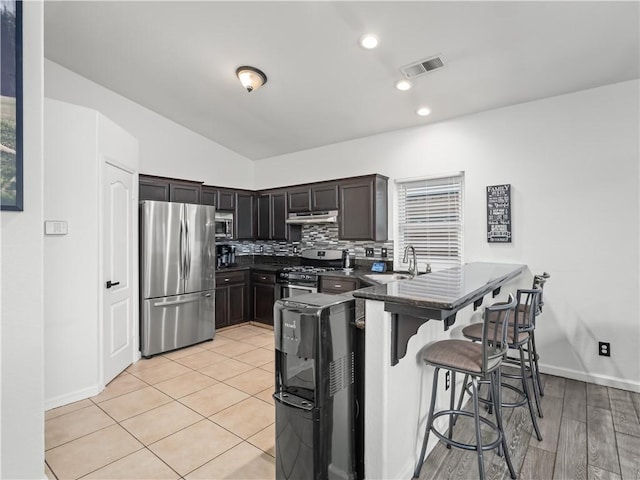 kitchen featuring stainless steel appliances, visible vents, a sink, a peninsula, and a kitchen bar