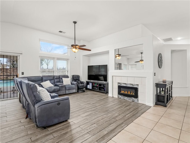 living room featuring visible vents, a fireplace, light wood-style flooring, and ceiling fan