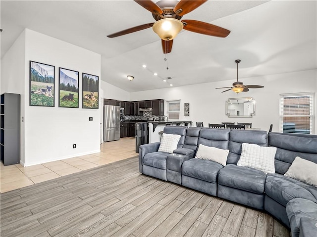 living area featuring vaulted ceiling, baseboards, a ceiling fan, and light wood-style floors