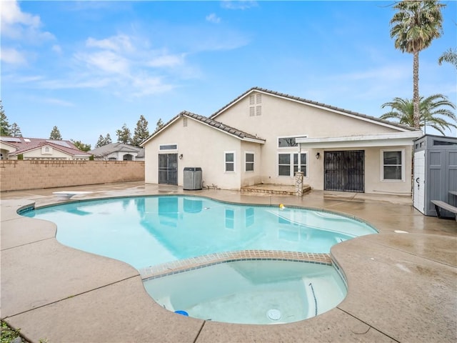 view of swimming pool with fence, a patio area, a pool with connected hot tub, a diving board, and central AC