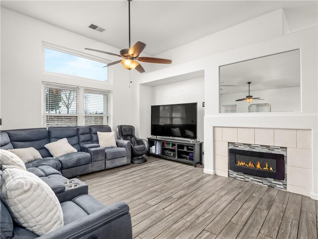 living area with visible vents, ceiling fan, a tiled fireplace, and wood finished floors