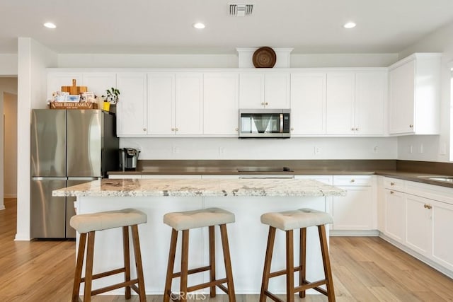 kitchen featuring appliances with stainless steel finishes, visible vents, light wood finished floors, and a kitchen bar